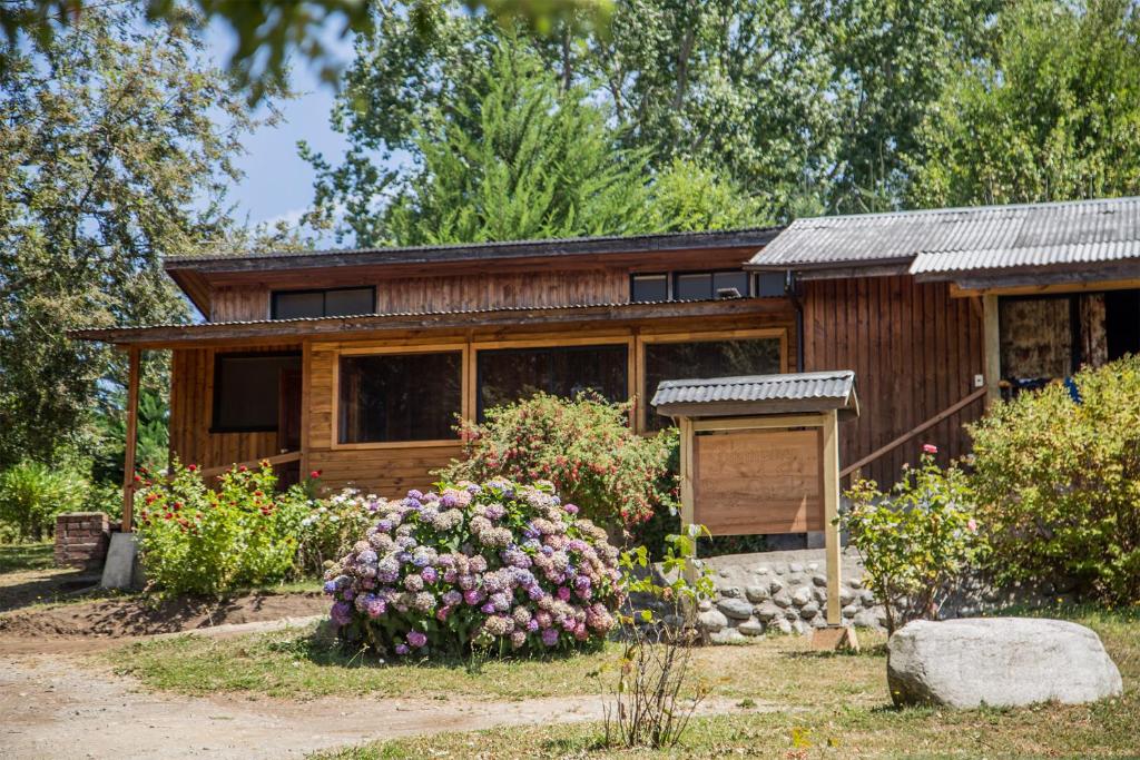 una piccola casa in legno con dei fiori di fronte di Refugio Ruka Cümelen a Panguipulli