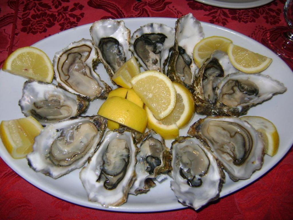 a plate of oysters and lemons on a table at Hotel Corsaro Nero in Portu Maga