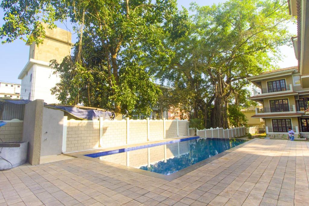 a swimming pool in front of a building with trees at Woodside Retreat- Serviced Apartments in Baga