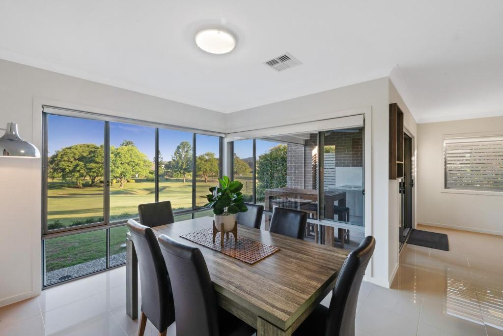 a dining room with a table and chairs and large windows at Fairway Village @ Windaroo Lakes Golf Club in Windaroo