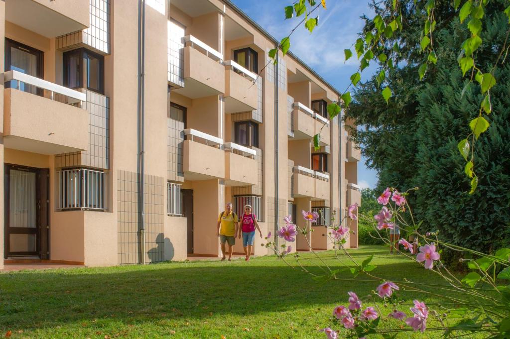 2 personnes marchant devant un bâtiment dans l'établissement Residence Routes du Monde ATC Bagneres de Bigorre, à Bagnères-de-Bigorre