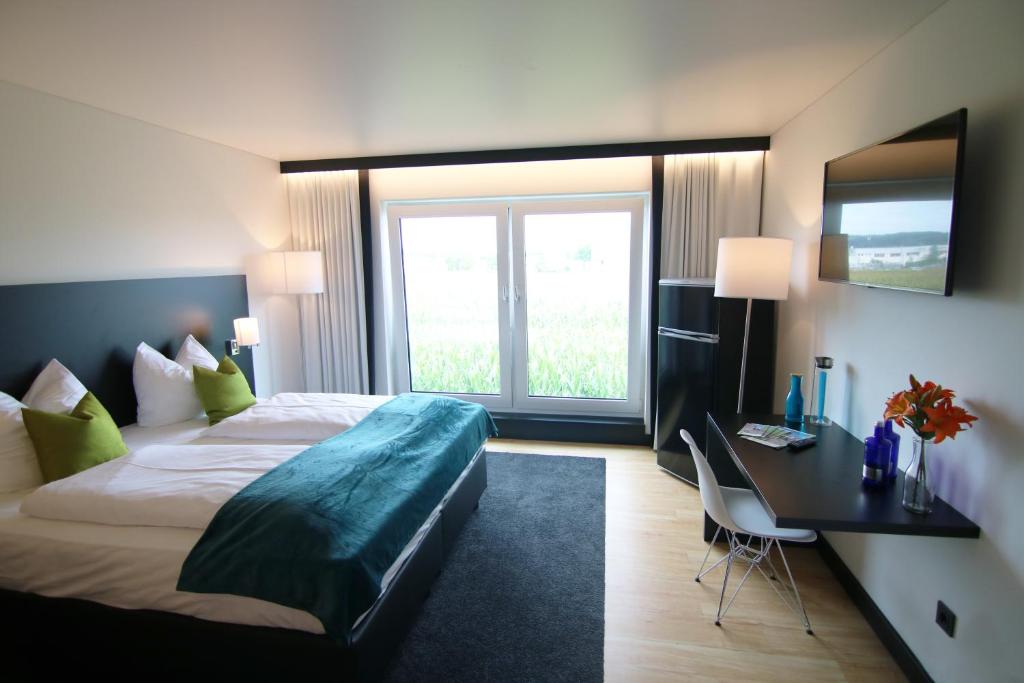 Habitación de hotel con cama y escritorio con ventana en ME Hotel by WMM Hotels en Meitingen