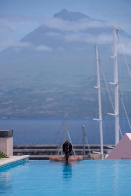 a person in a swimming pool with a boat in the water at Azoris Faial Garden – Resort Hotel in Horta