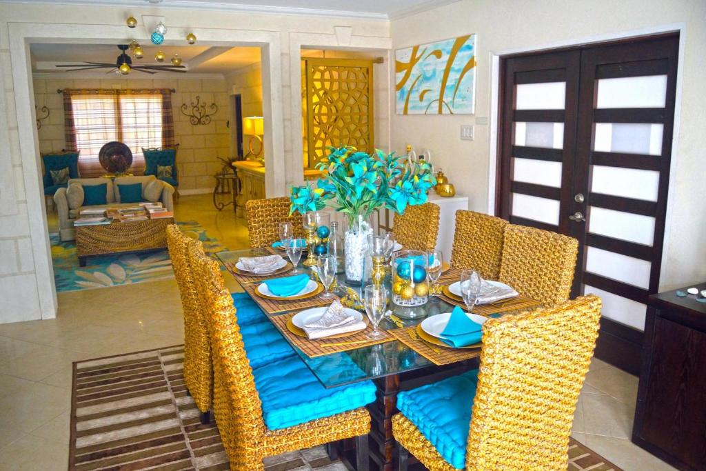 a dining room table with yellow wicker chairs and a blue table cloth at Hidden Gem Barbados in Christ Church