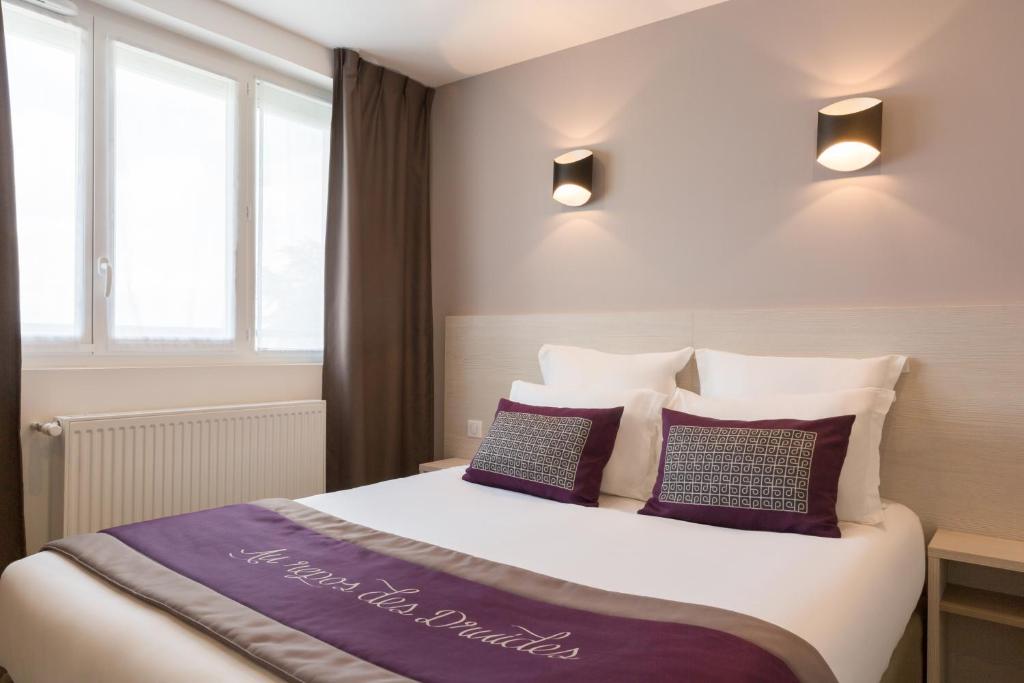 a bedroom with a large bed with purple pillows at The Originals City, le Relais des Carnutes Brezolles Verneuil sur Avre in Brezolles