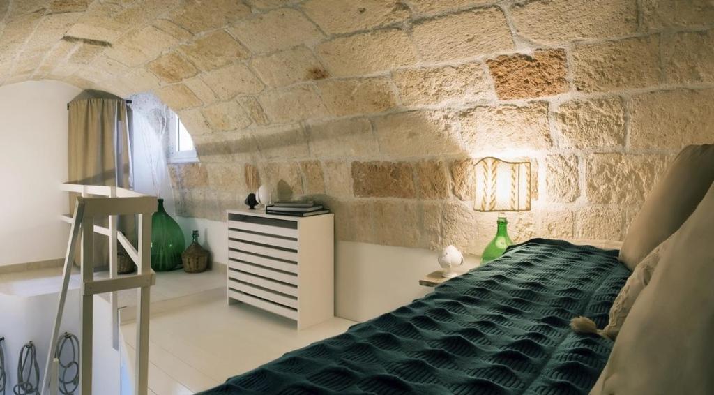 a bedroom with a stone wall with a bed and a table at Allure 84 - Little Gem in the heart of the old town in Polignano a Mare