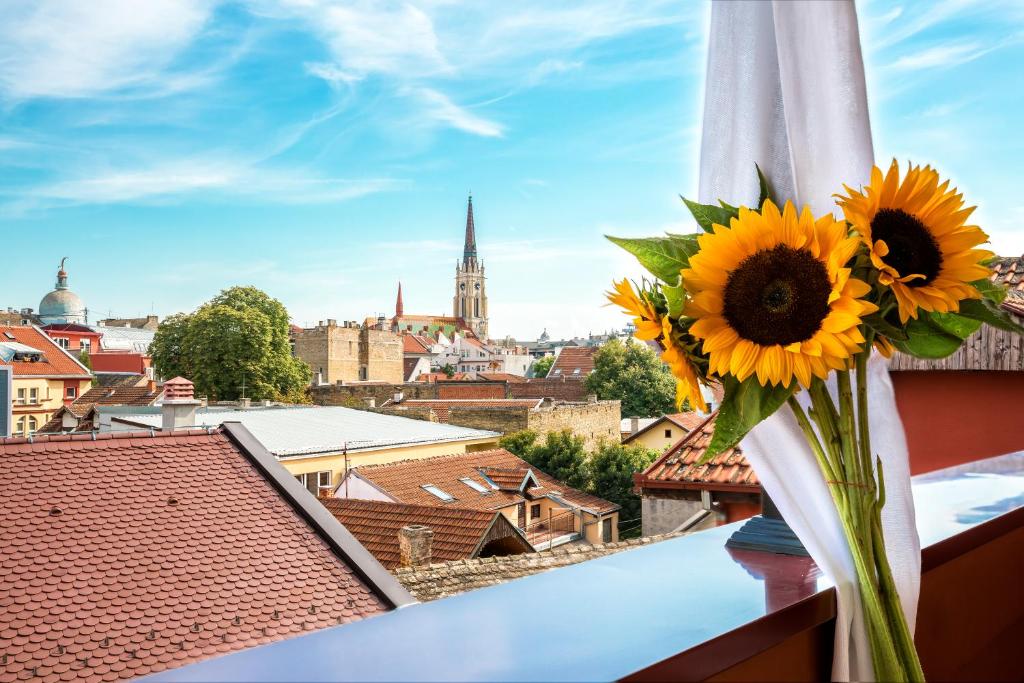 un jarrón lleno de girasoles sentado en una cornisa con una ciudad en Hotel Fontana en Novi Sad