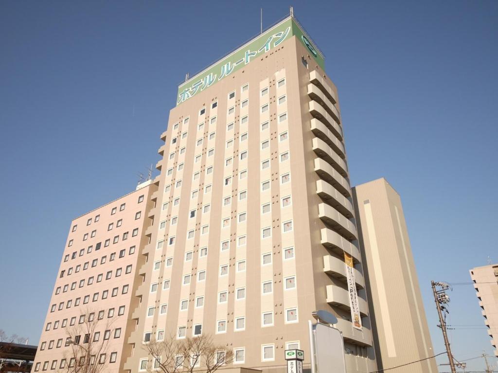 a tall tan building with a green sign on it at Hotel Route-Inn Gifuhashima Ekimae in Hashima