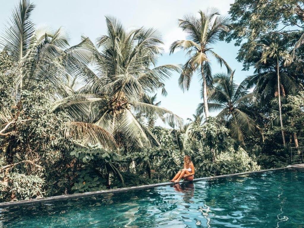 una donna seduta in una piscina di fronte alle palme di Good Vibes Villas a Unawatuna