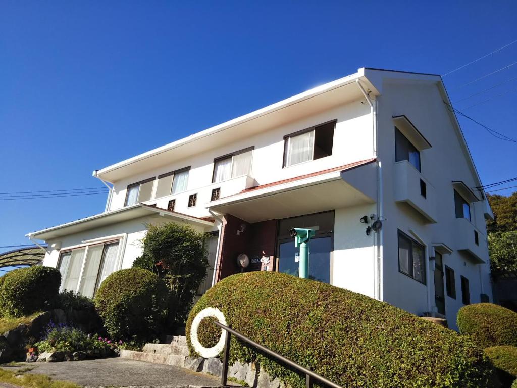 a white building with bushes in front of it at ペンションみかんの郷 in Bizen