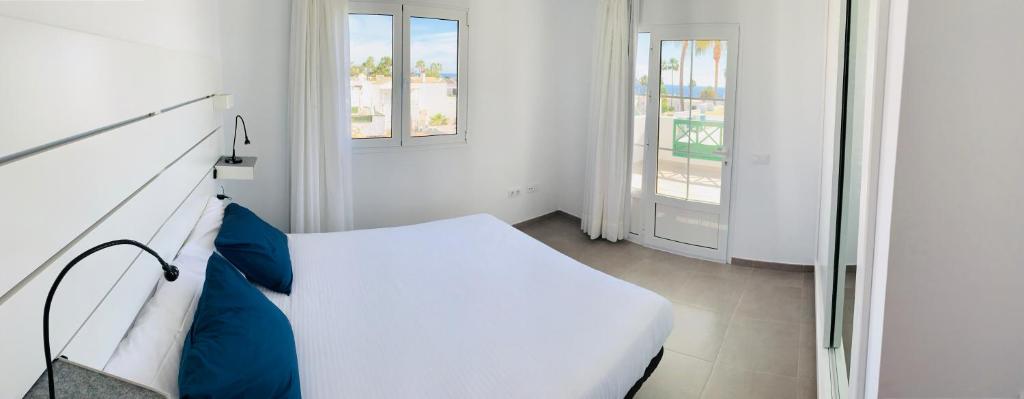 a white bedroom with a bed and two windows at Apartamentos Zalabar in Tías