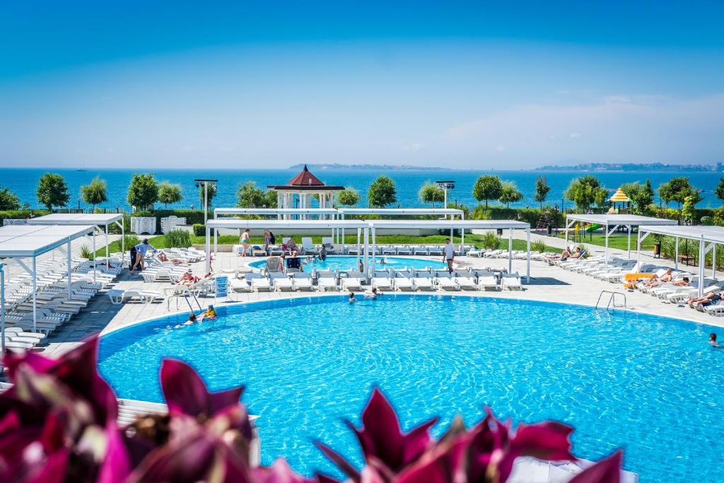 a large swimming pool with lounge chairs and the ocean at Premier Fort Beach Resort in Sunny Beach