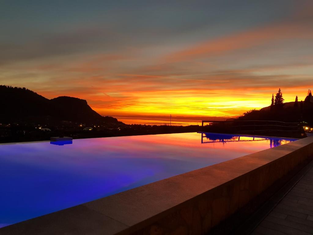 a swimming pool with a sunset in the background at Relais Villa Olivi in Costermano