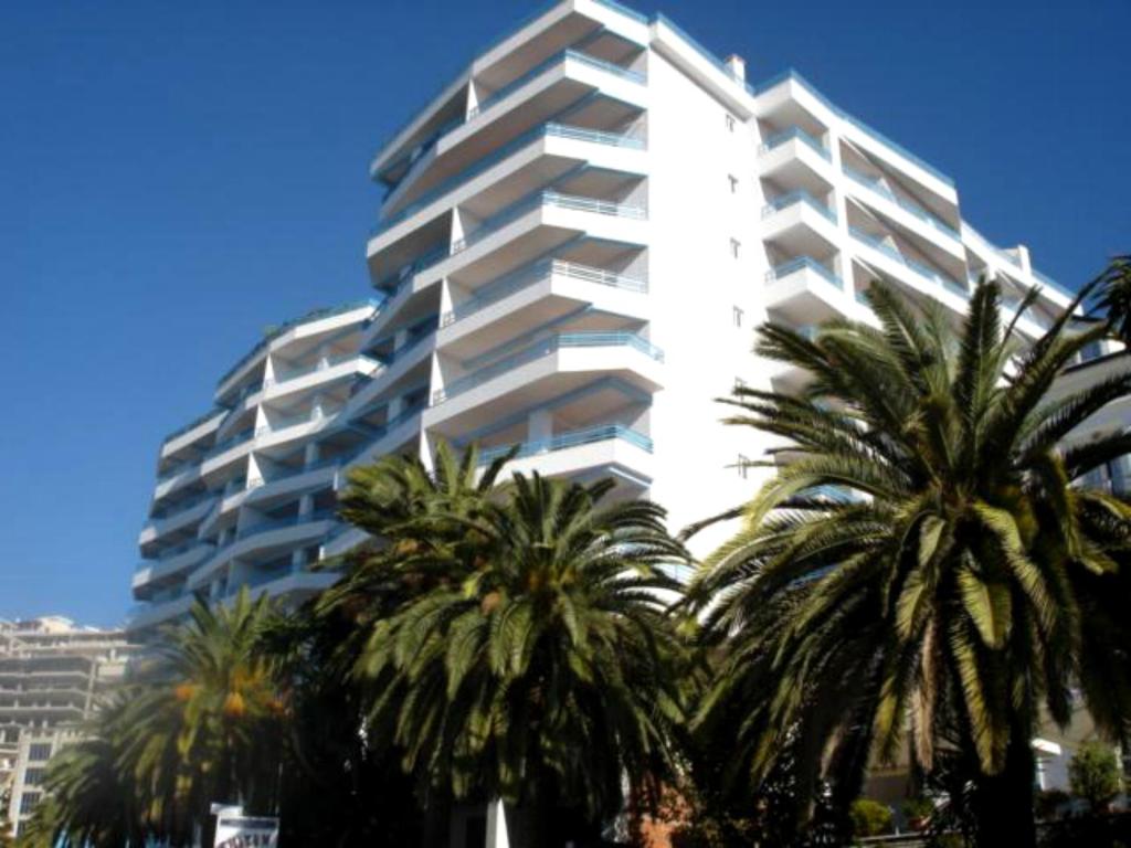 a tall white building with palm trees in front of it at Apartments Serxhio in Sarandë