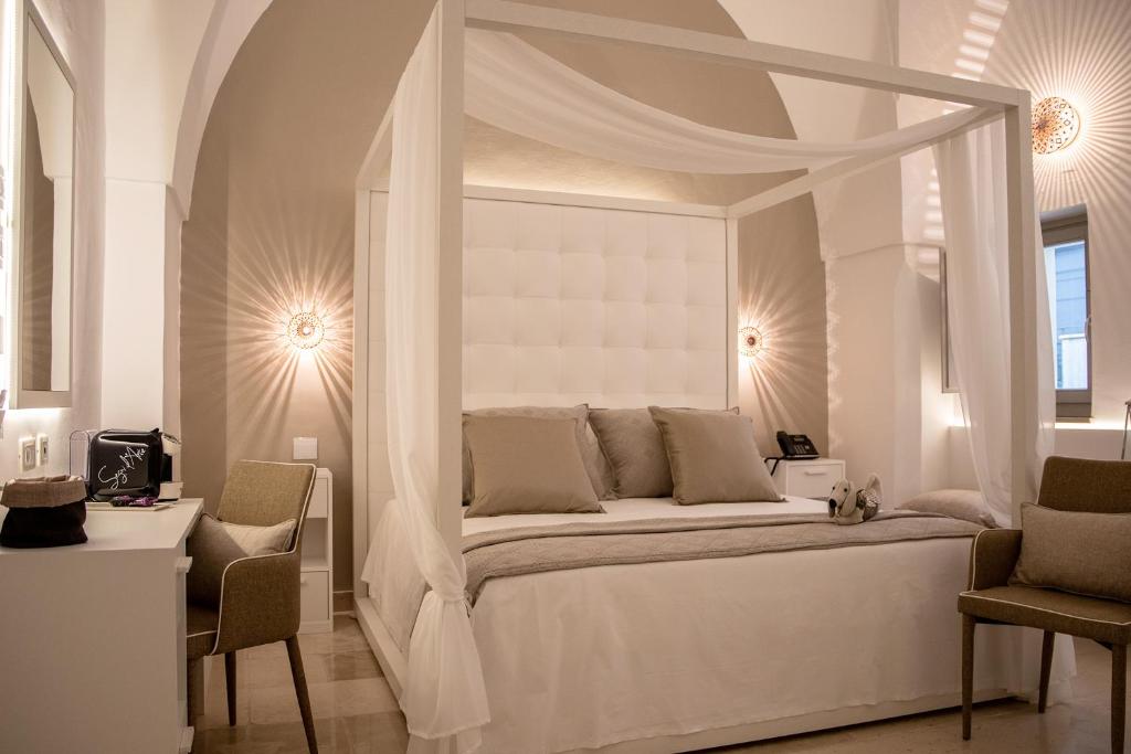 a white bedroom with a canopy bed with two chairs at MONUN Hotel&Spa in Grottaglie