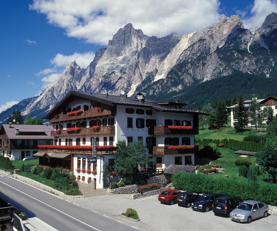 a building with cars parked in front of a mountain at Hotel Albergo Dolomiti in San Vito di Cadore