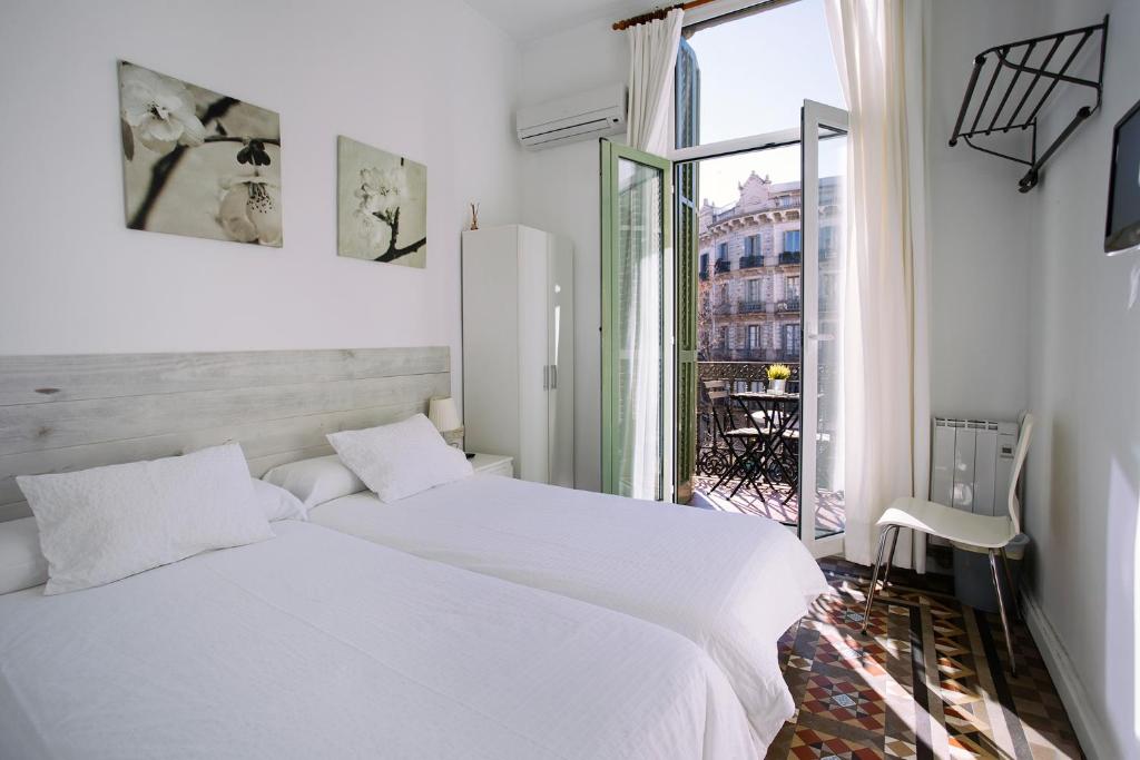 a white bedroom with two beds and a window at Hostal Eixample in Barcelona