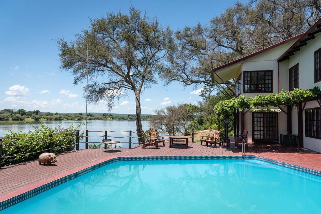 a swimming pool next to a house with a lake at Kayube Zambezi River House in Livingstone