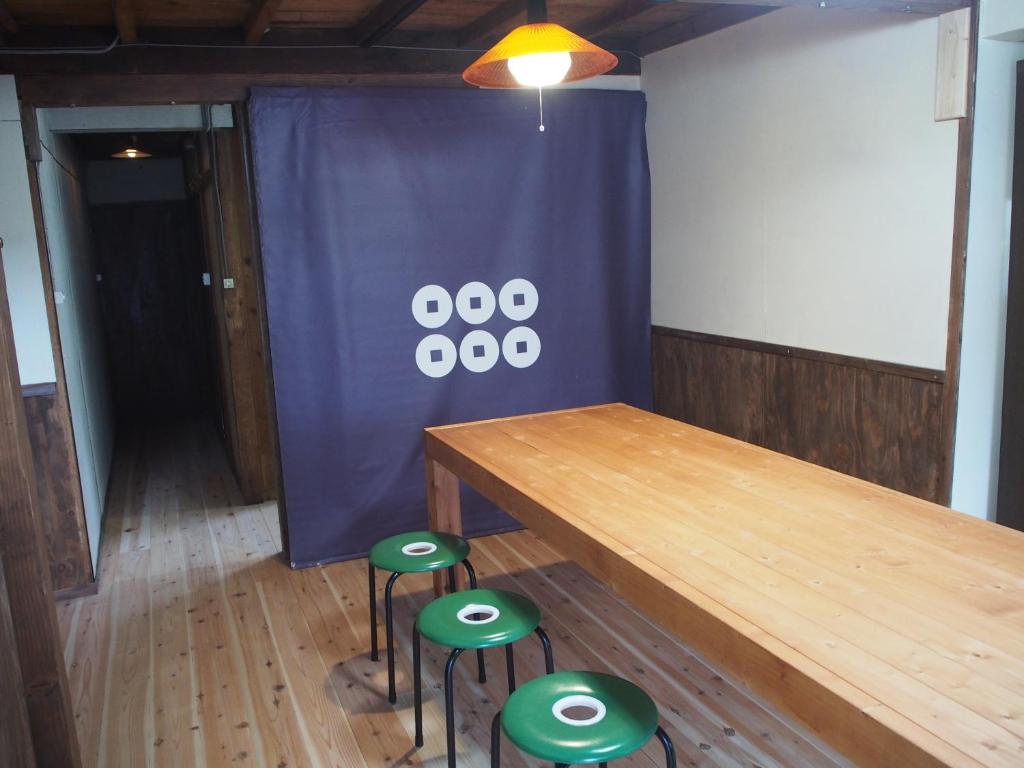 una sala de conferencias con mesa de madera y taburetes verdes en Guesthouse Matsushiro Walkers, en Nagano