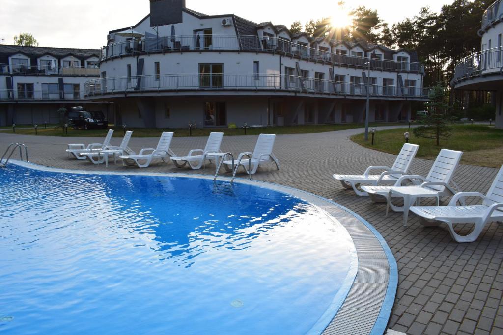 a pool with lounge chairs and a building in the background at Apartamenty Silence Baltic Pod Żaglami in Pobierowo