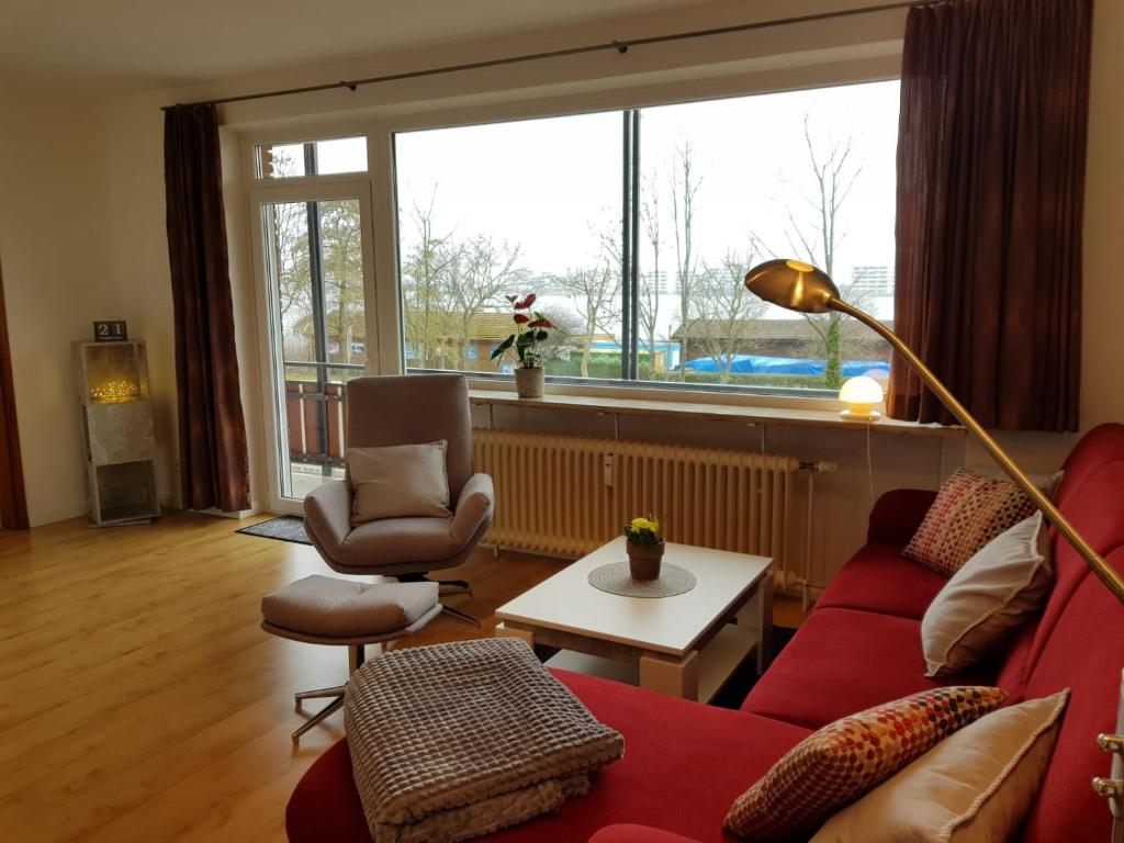 ein Wohnzimmer mit einem roten Sofa und Stühlen sowie einem großen Fenster in der Unterkunft Stadtdomizil am Binnensee, Haus Bellevue in Heiligenhafen