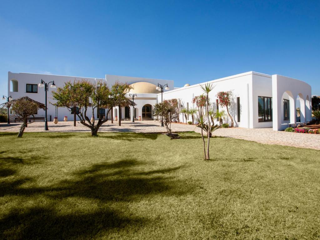 a white building with trees in front of a yard at Zahira Resort in Tre Fontane