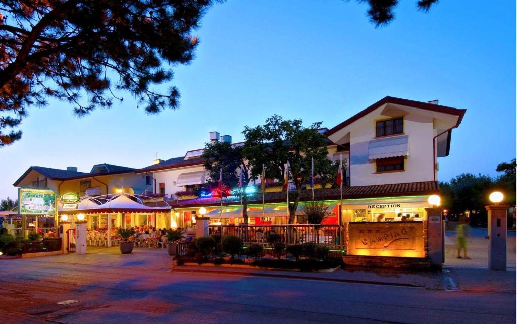 a building with tables and umbrellas on a street at night at Camping Parco Capraro in Lido di Jesolo