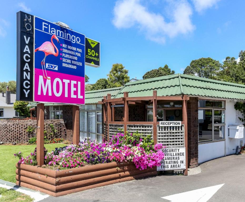 a motel with a sign and flowers in front of it at Flamingo Motel in New Plymouth