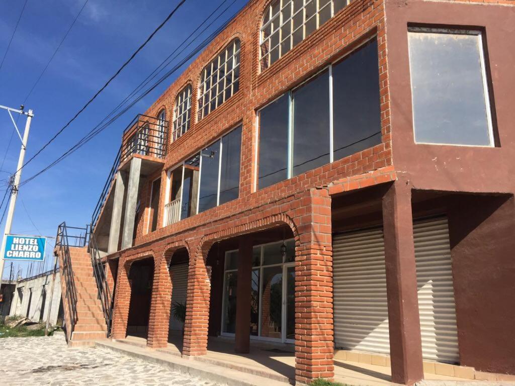 a red brick building with large windows on a street at Hotel Lienzo Charro II in San Miguel Regla