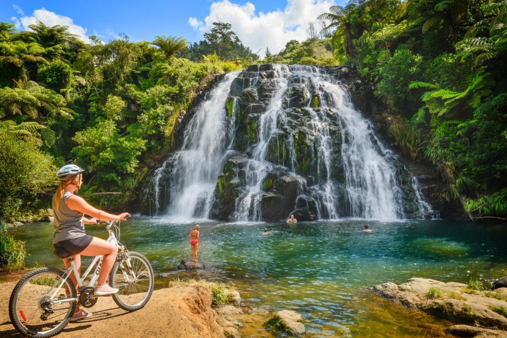 a woman riding a bike in front of a waterfall at Riverside Accommodation in Karangahake