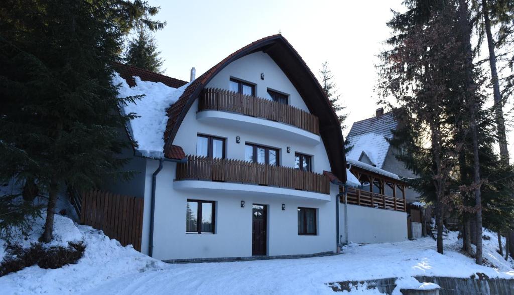 a white house with a gambrel roof in the snow at Homoród Kulcsosház in Băile Homorod