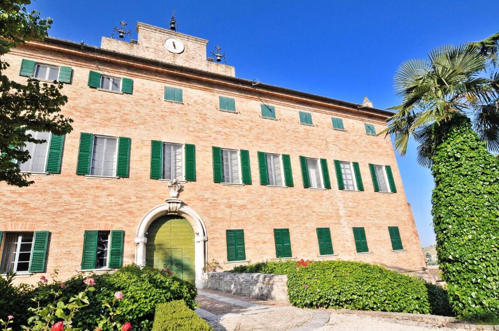 een groot bakstenen gebouw met groene luiken en een klokkentoren bij Castello Di Monterado in Monterado