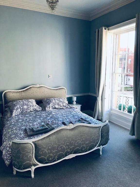 a bedroom with a bed with blue walls and a window at Regency Rooms Guesthouse in Cheltenham