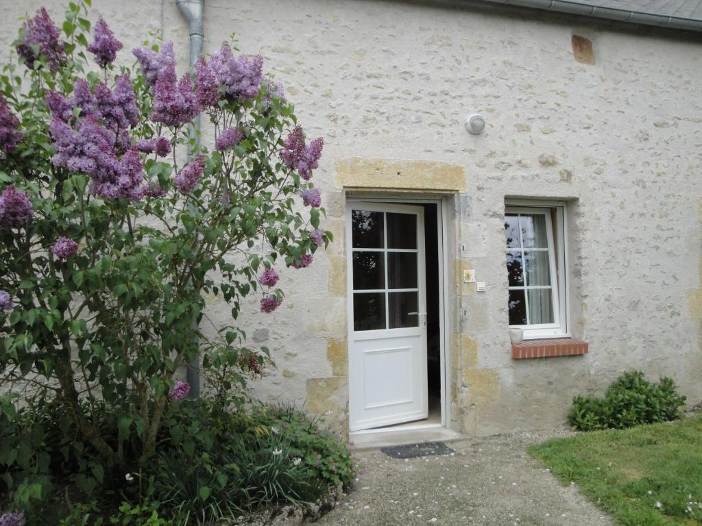 una casa con una puerta blanca y un arbusto con flores púrpuras en Gite à la ferme de La poterie en Donnery