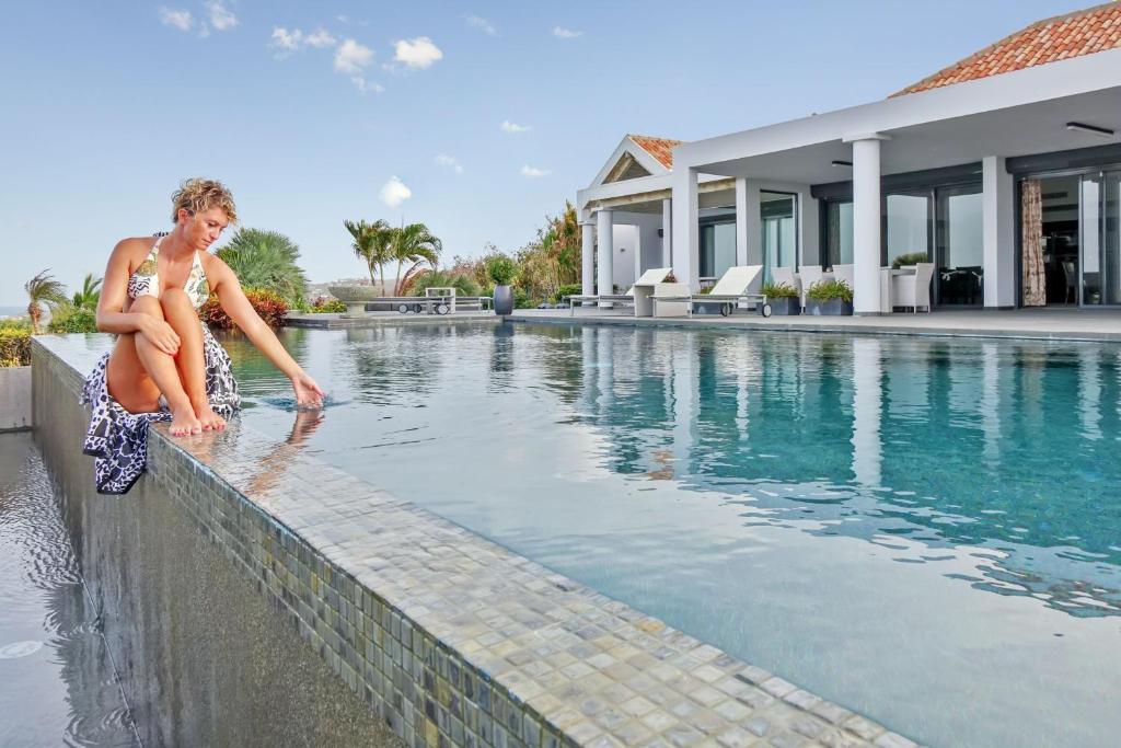 a woman sitting on a wall next to a swimming pool at Villa Dolphin Saint Martin in Orient Bay