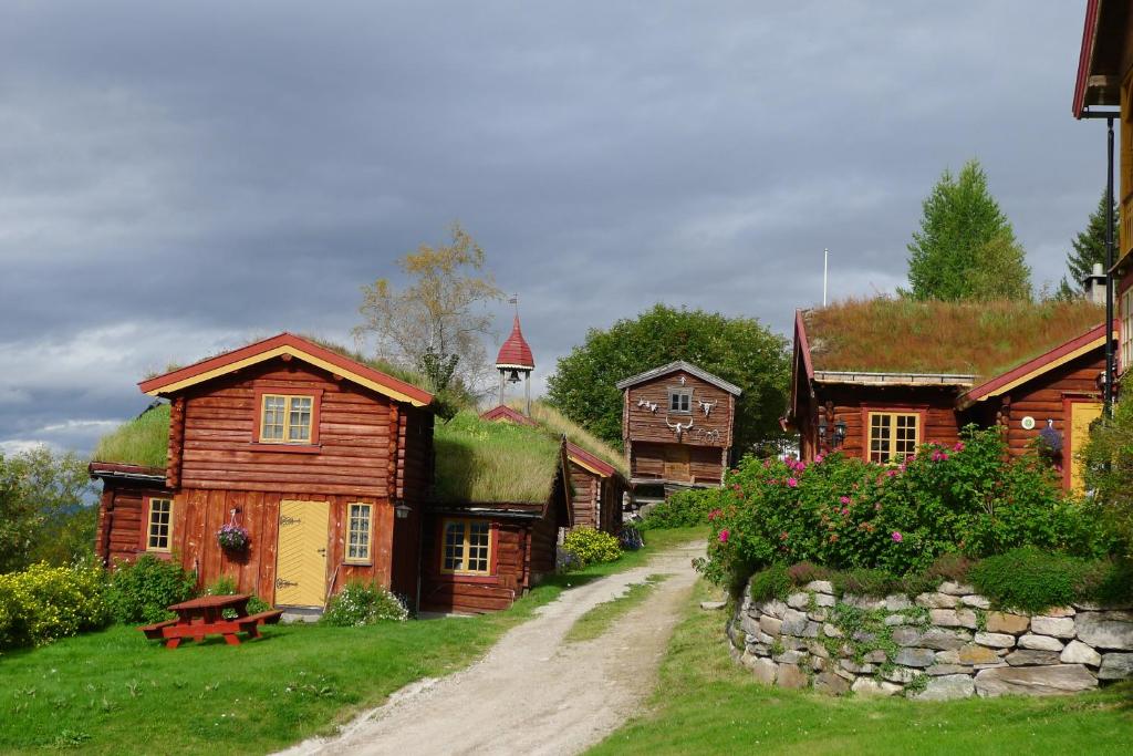 um grupo de casas com telhados de relva e uma estrada de terra em Romenstad Hytter em Rendalen