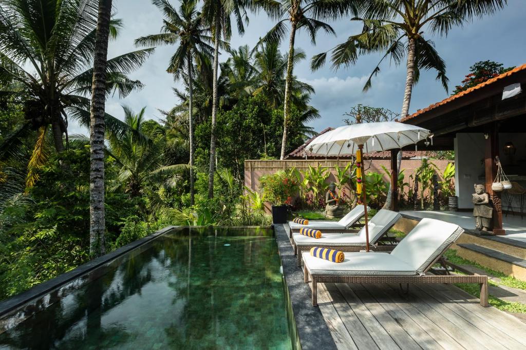 einen Pool mit Liegestühlen und einem Sonnenschirm in der Unterkunft Villa Niyamas Ubud in Ubud