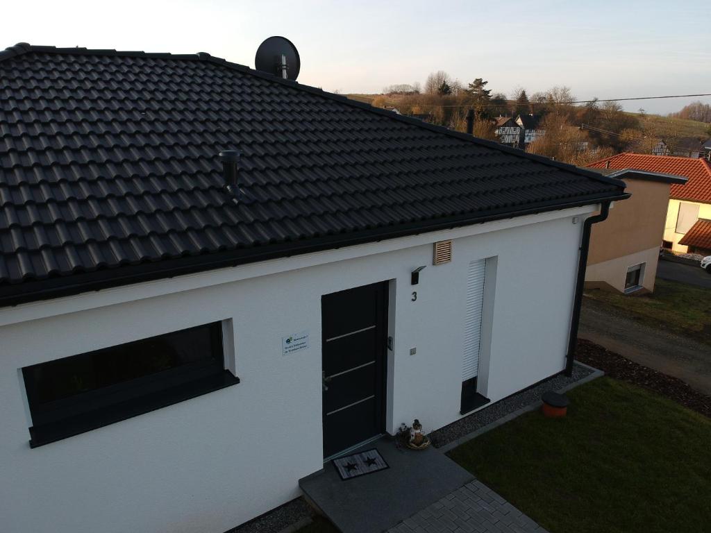 a white building with a black door and a roof at Ferienhaus Stricker in Birken-Honigsessen