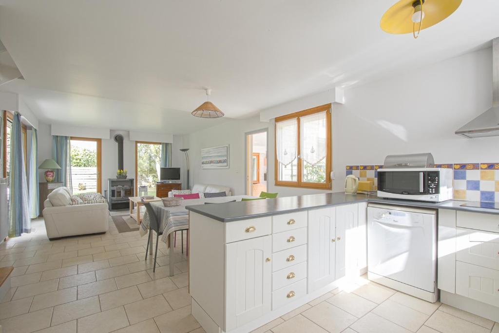 a kitchen with white cabinets and a living room at Les Costils in Saint-Laurent-sur-Mer