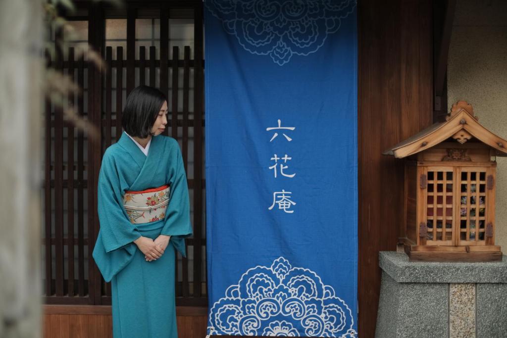a woman in a blue robe standing in front of a banner at 京都 六花庵 Kyoto Rokkaan in Kyoto