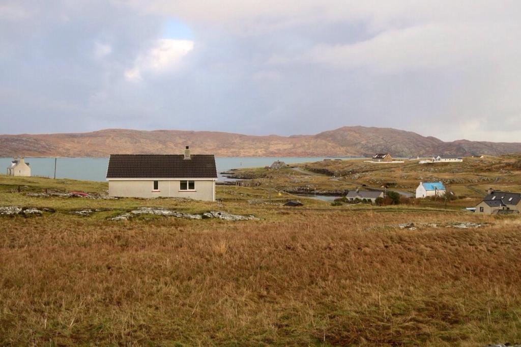 a small white house in a field with a body of water at Sealladh A’ Chaolais (Eriskay) in Eriskay