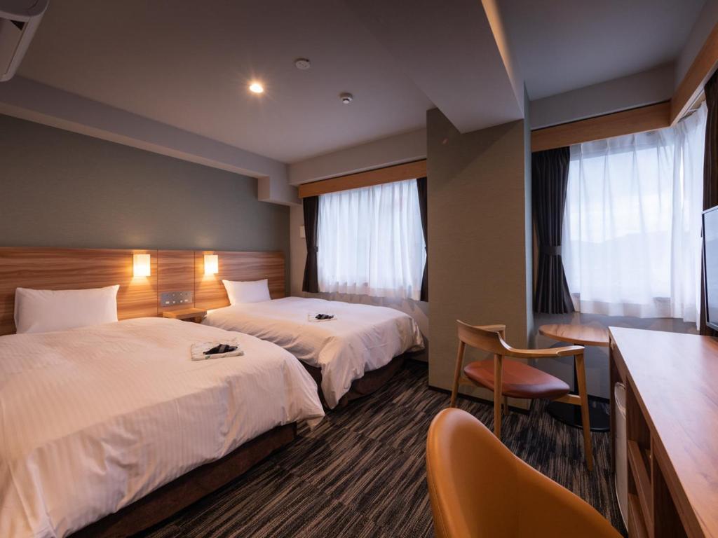 a hotel room with two beds and a desk at Central Hotel Takeoonsen Ekimae in Takeo