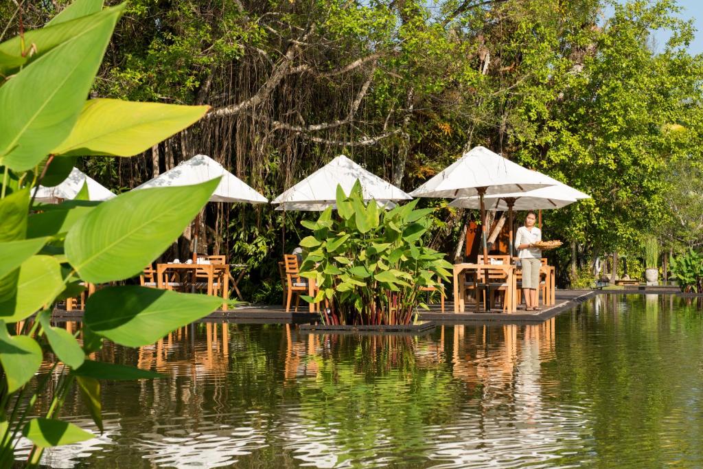 a man standing in front of tables and umbrellas by the water at The Sarojin in Khao Lak
