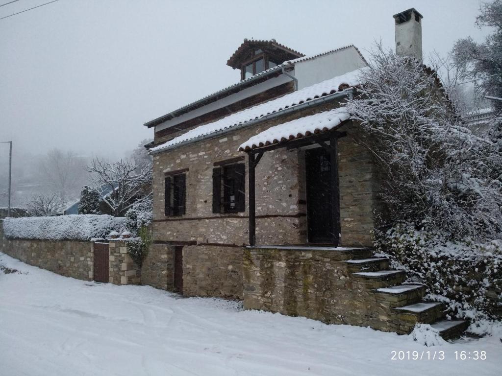 un pequeño edificio de piedra en la nieve con nieve en Traditional Greek Cottage en Palaiókastron