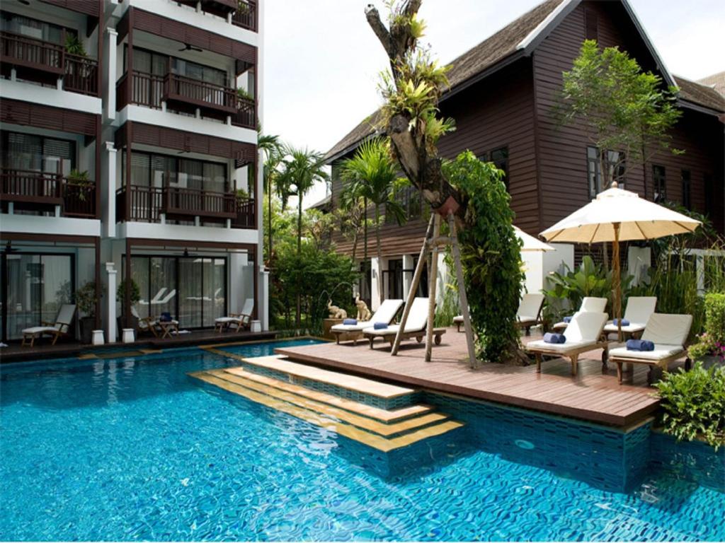 una piscina con sillas y una sombrilla junto a un edificio en Rarin Jinda Wellness Spa Resort en Chiang Mai