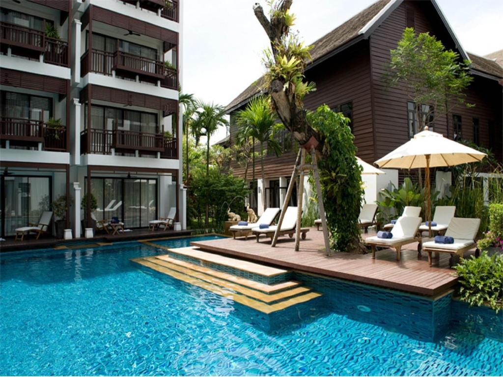 清邁的住宿－拉林金達溫泉度假酒店，一座带椅子和遮阳伞的游泳池位于大楼旁