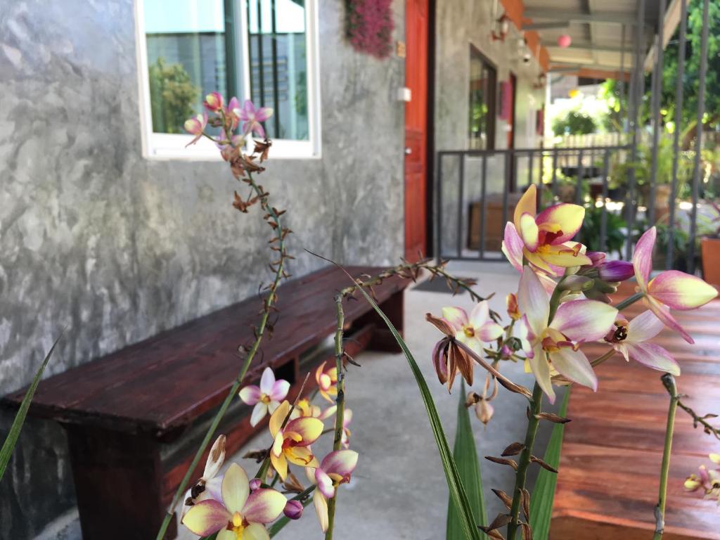 eine Vase voller Blumen neben einer Holzbank in der Unterkunft Muangchaem House in Mae Chaem