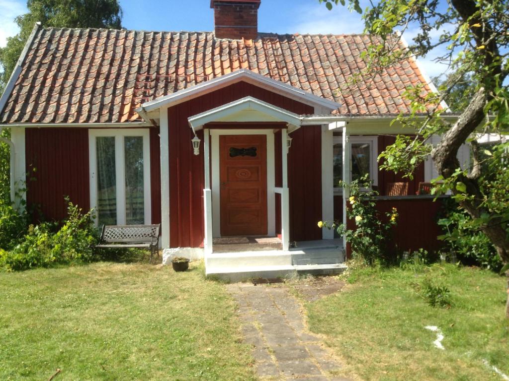una pequeña casa roja con una puerta y un banco en Rosendahl en Ålem