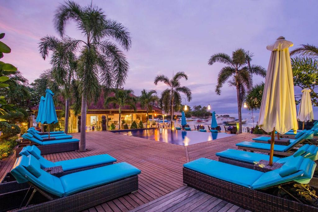 a pool with blue lounge chairs and umbrellas at Bay Shore Huts in Nusa Lembongan