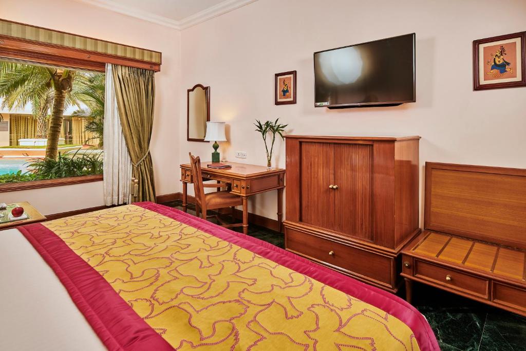 a bedroom with a bed and a desk and a television at The Ummed Ahmedabad Airport in Ahmedabad